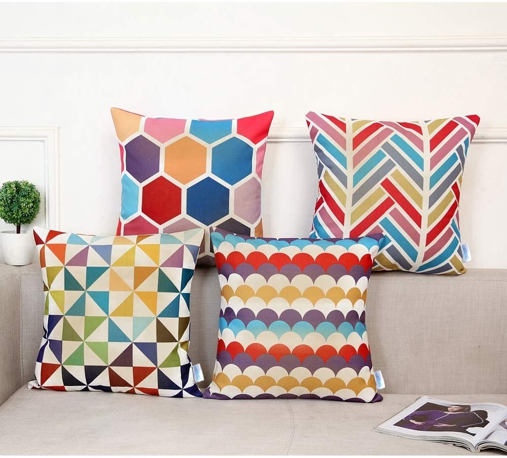 A grey couch with four colorful, pattern-covered pillows on it: one has a honeycomb pattern, one a chevron, one a pinwheel and one a fishscale. 