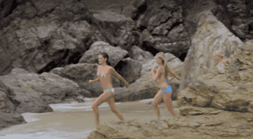 Three girls running into the ocean wearing bikinis