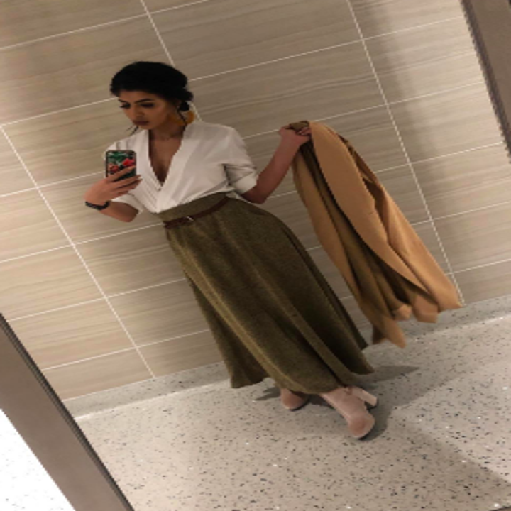 Reviewer wearing skirt with brown belt and low cut white blouse 