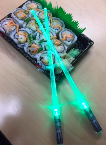 Green lightsaber chopsticks on top of tray filled with spicy crab sushi rolls