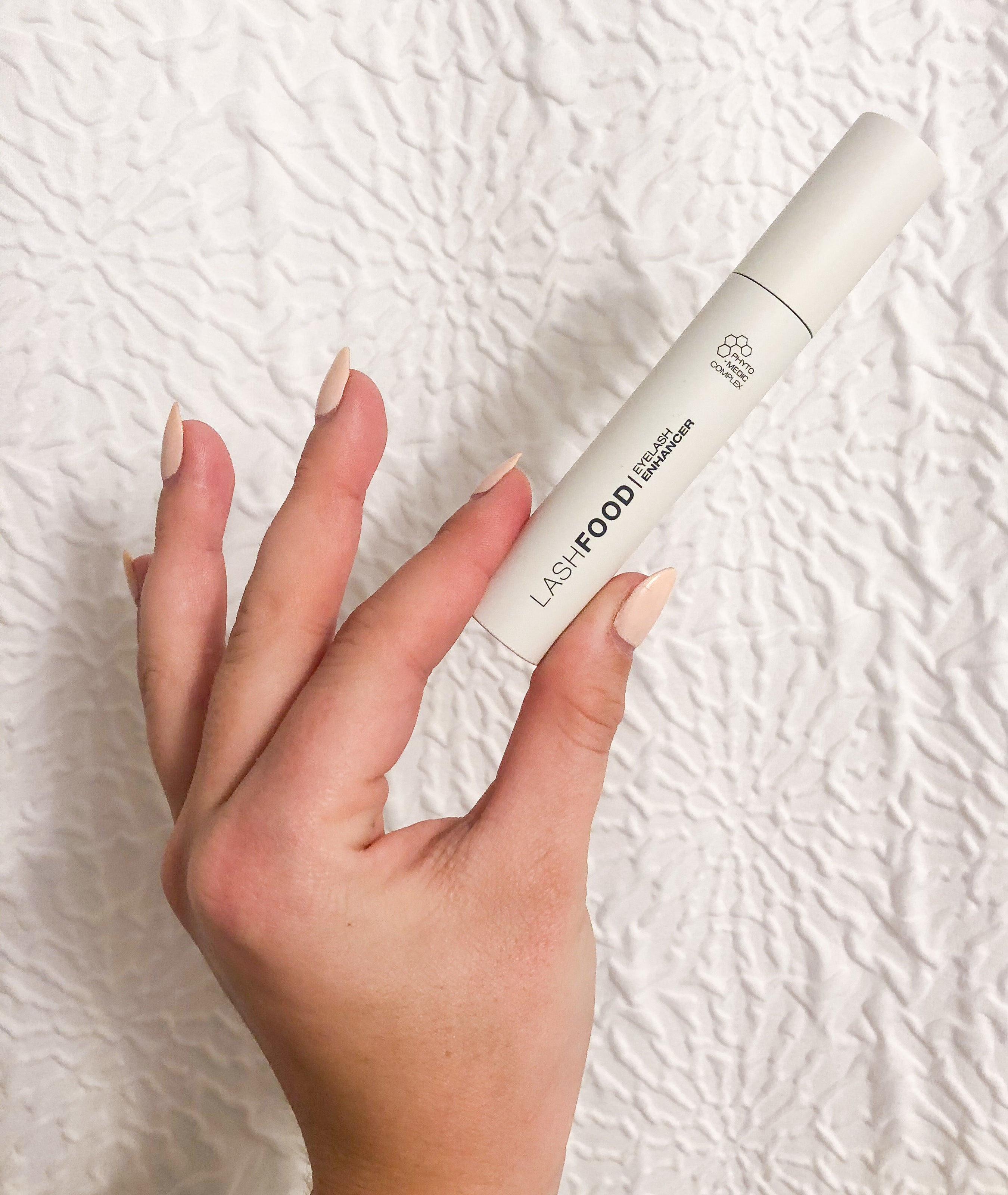 A person holds the lash conditioner between their fingers against a graphic backdrop