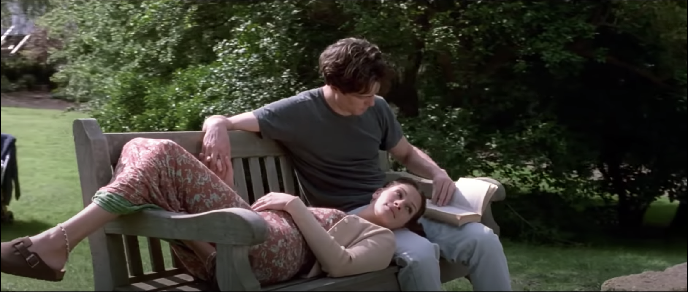 Hugh as Will Thacker sitting on a bench reading to Julia Roberts as Anna Scotts in Notting Hill