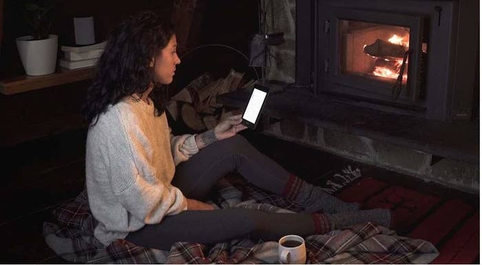 A person reading on their Kindle in front of a fireplace at home.