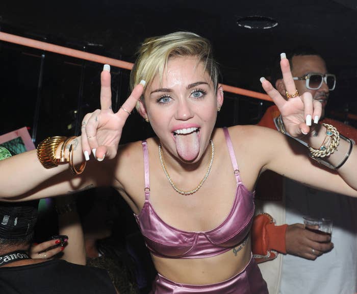 Miley at a party sticking out her tongue and making the peace sign