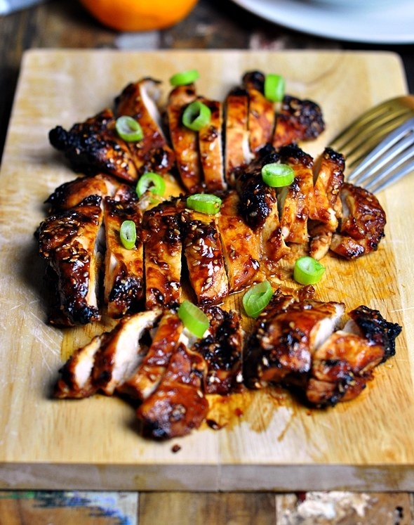 Sliced marinated chicken breast on a cutting board topped with scallions.