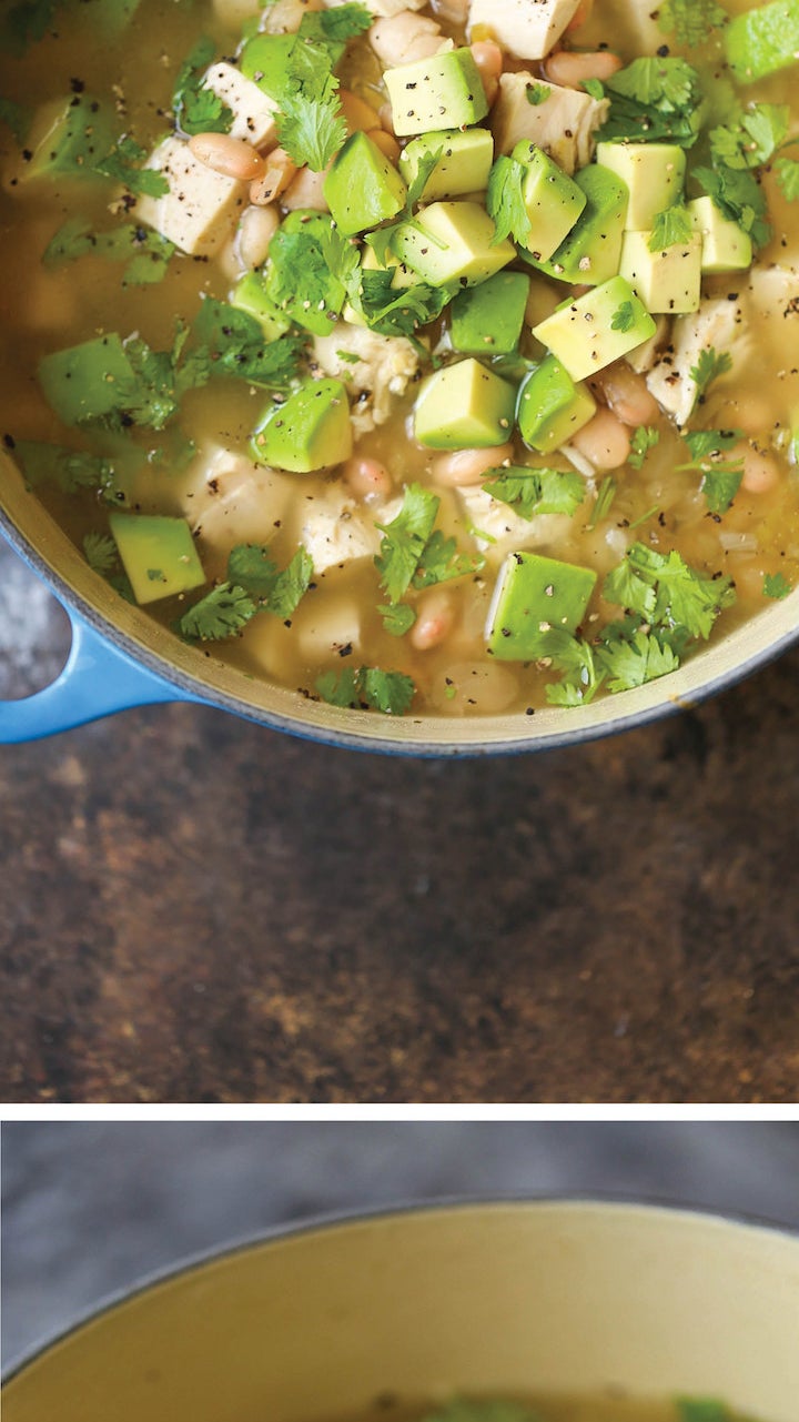 A Dutch oven filled with chunky chicken and white bean stew with avocado and cilantro