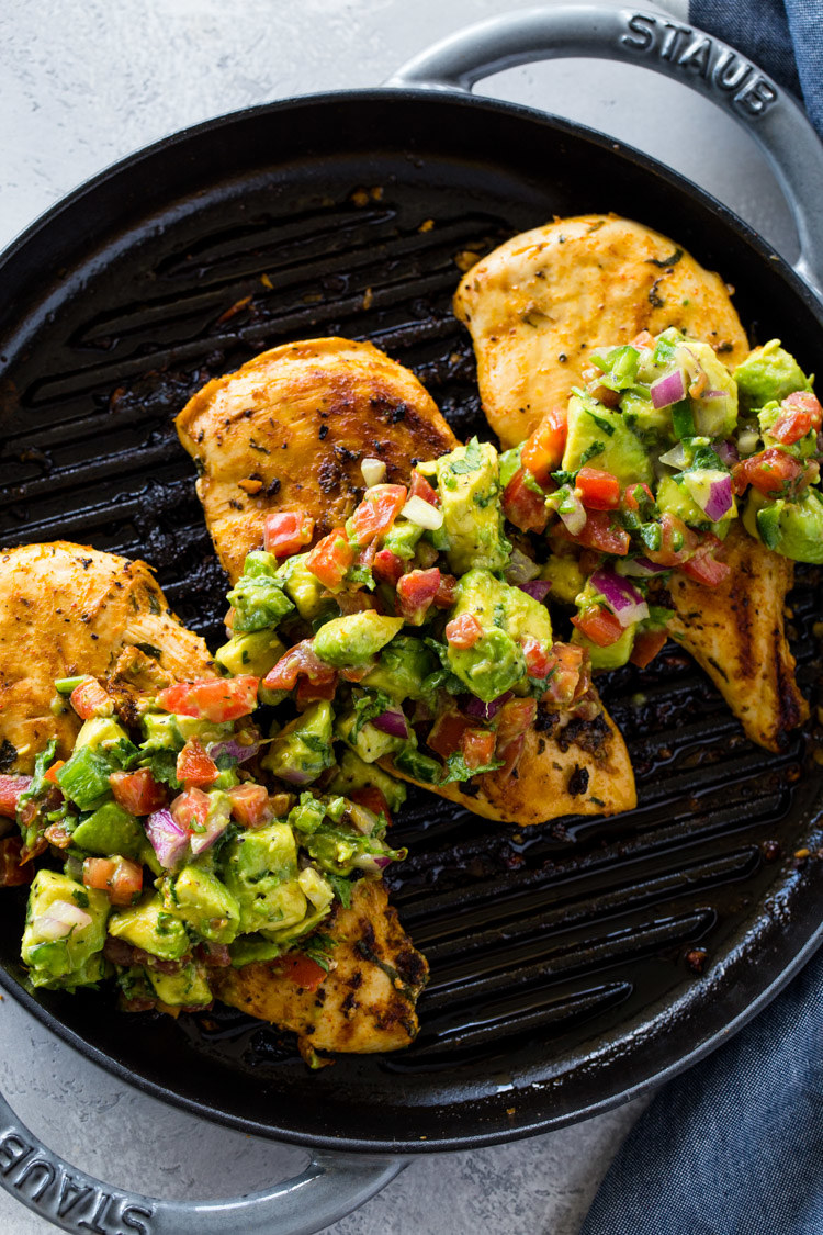 Three grilled chicken breasts in a griddle pan topped with avocado salsa