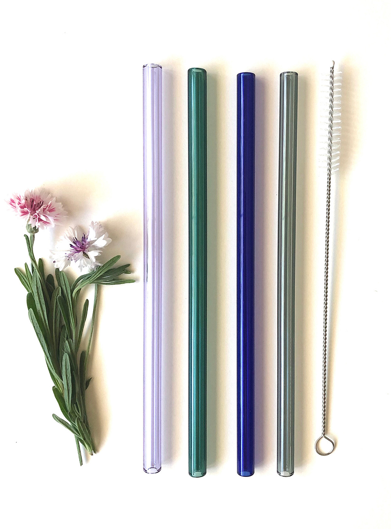 A set of four glass straws and a small cleaning brush on a plain background