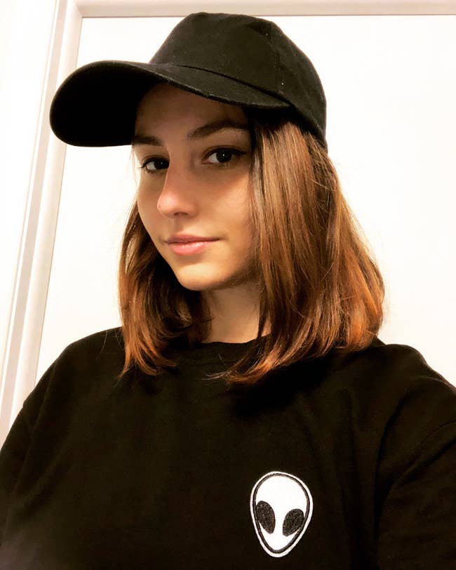 buzzfeed writer wearing a black baseball cap and black sweatshirt with an alien patch on the front