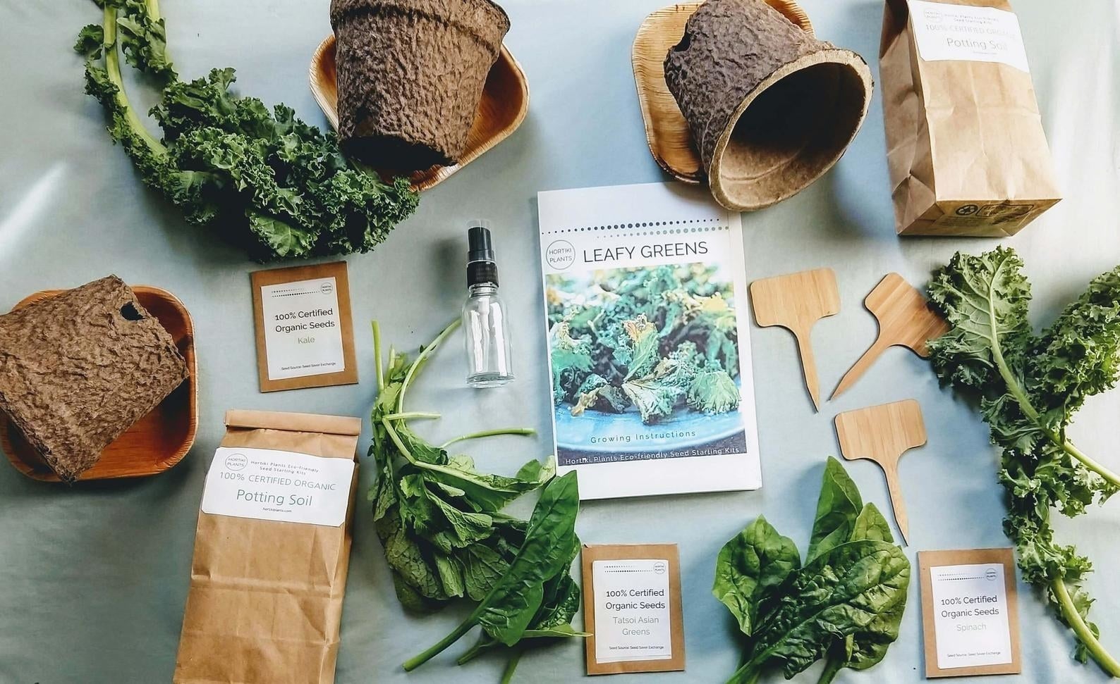An instruction packet that reads "Leafy Greens" surrounded by a collection of pots, trays, soil, and seed packets
