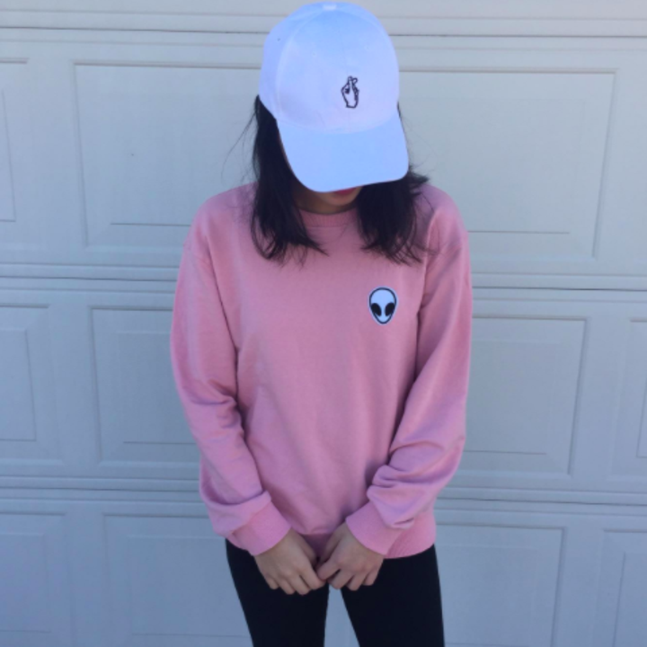 Reviewer wears same style sweatshirt in a pink color with a white baseball cap and leggings