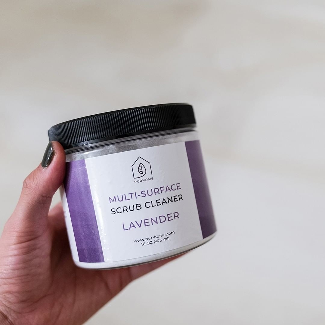 A hand holding a tub of the scrub in the lavender scent