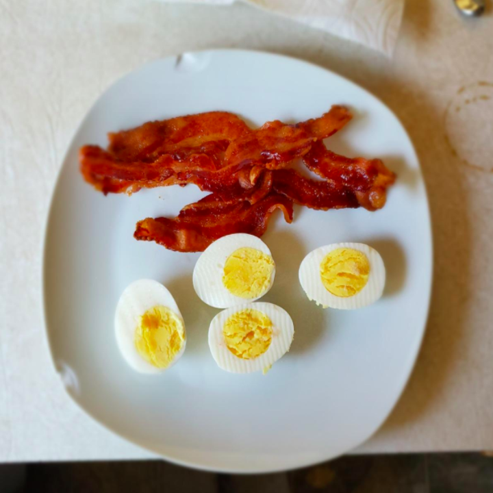A reviewer photo of hard boiled eggs that were made in the cooker on a plate with bacon