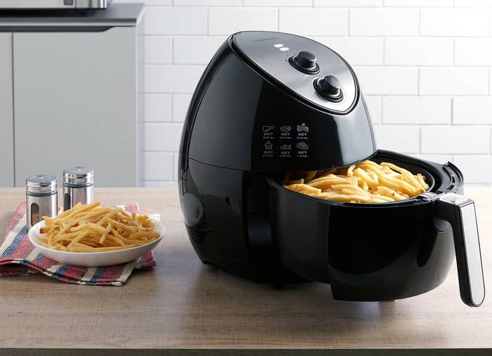 Black air fryer on a counter with fries in the fryer basket