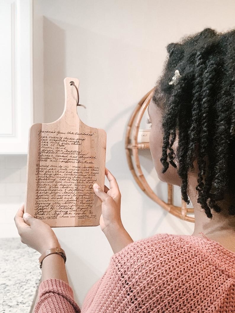 A model holding the cutting board, which is about the size of a piece of paper with the recipe engraved in cursive