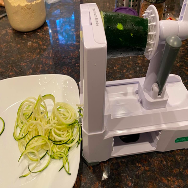 A zucchini inside the spiralizer with some spiralized zucchini on a plate next to it