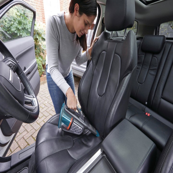 person using handheld vacuum to vacuum her car
