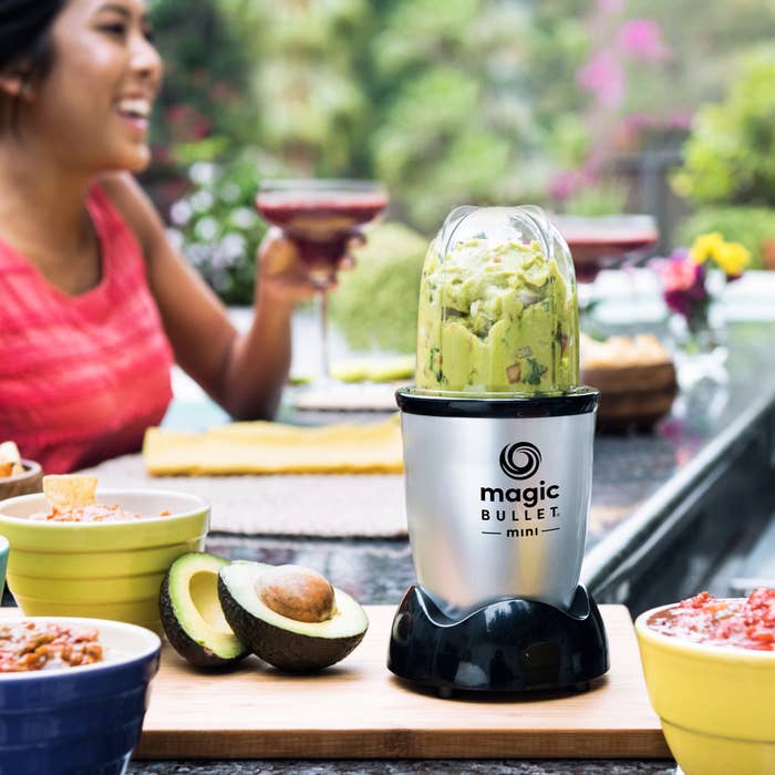 magic bullet mini blender with guacamole in it with a person drinking a cocktail in the background