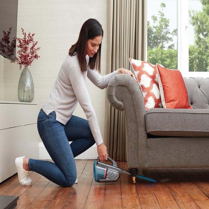 person using handheld vacuum to clean under couch