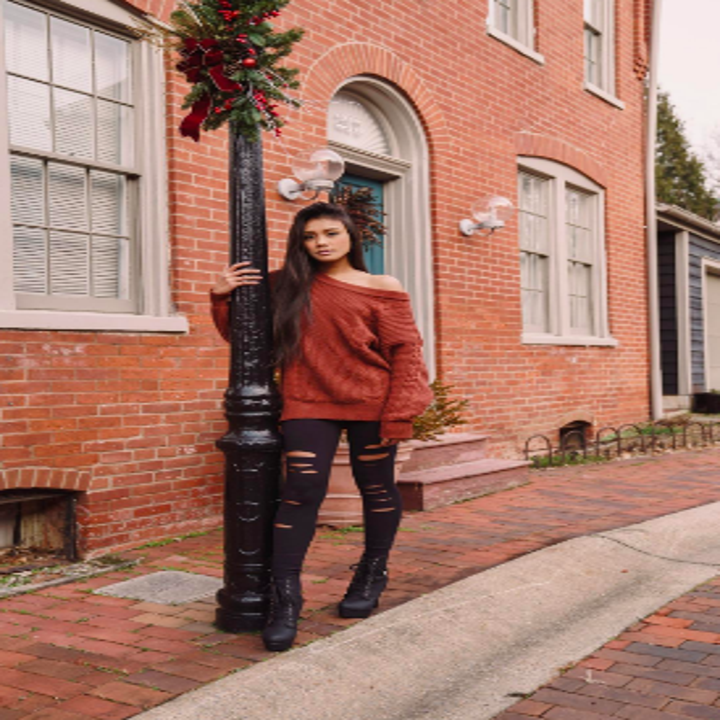 Reviewer wearing sweater in burnt orange. It's worn off-the-shoulder with black torn jeans.