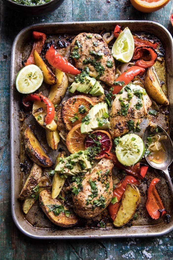 Roasted chicken with potato wedges, peppers, and onions covered in herbs on a sheet pan