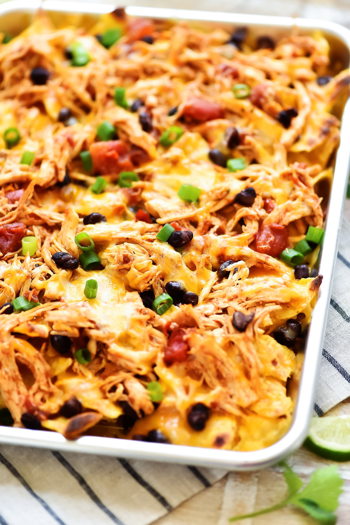 A sheet pan of cheesy nachos topped with shredded chicken, black beans, tomato, and green onions
