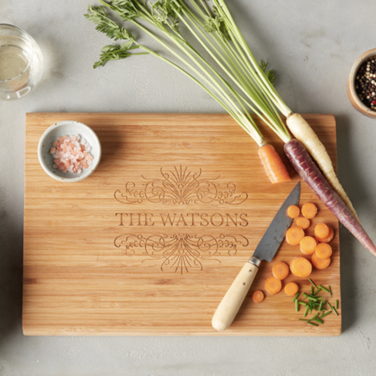 The brown wood square cutting board with the words "The Watsons" and a design above and below the name