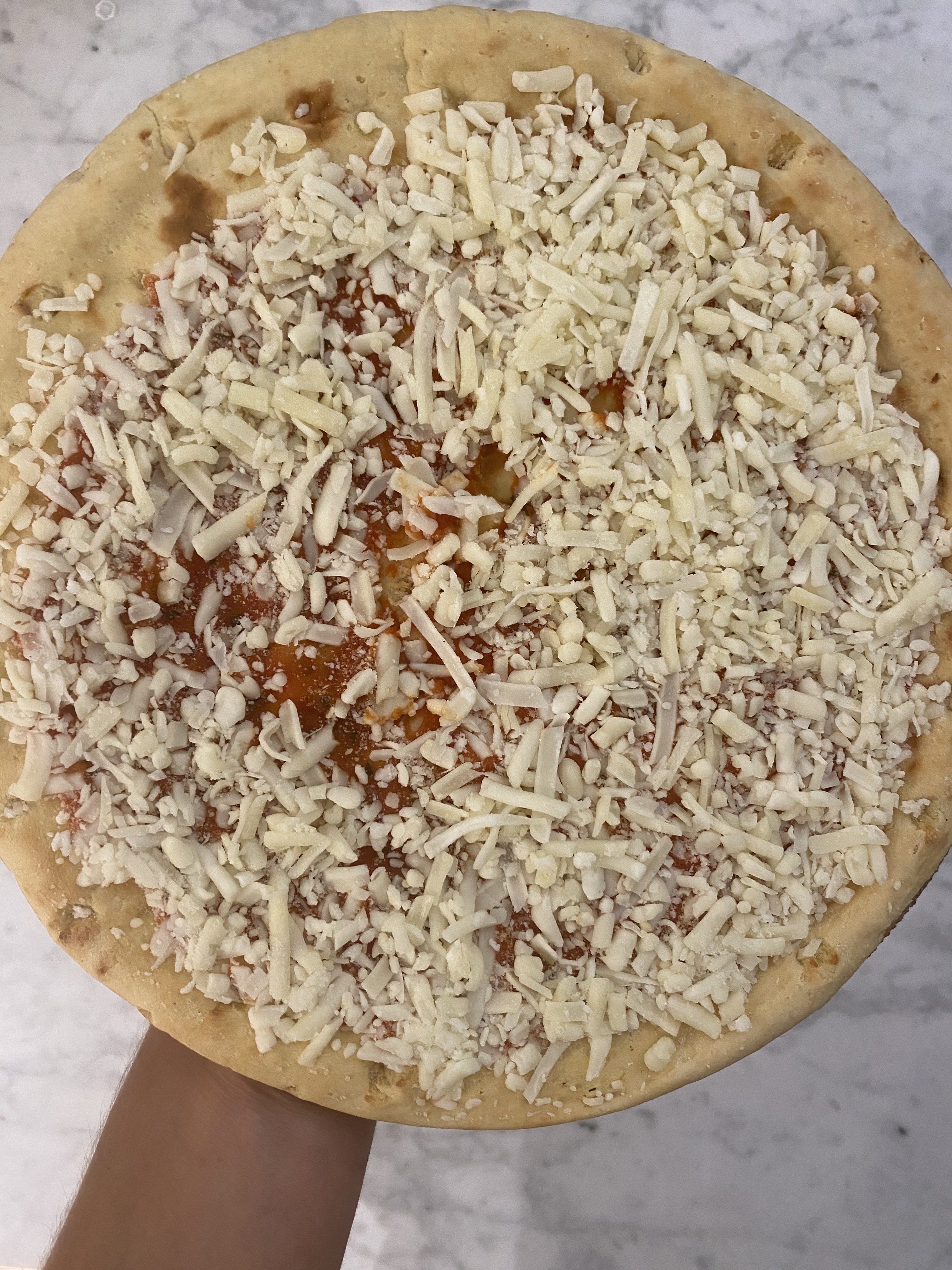 A frozen Banza chickpea pizza covered with shredded cheese.