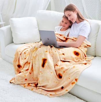 Models sit on white couch with blanket that looks like a tortilla