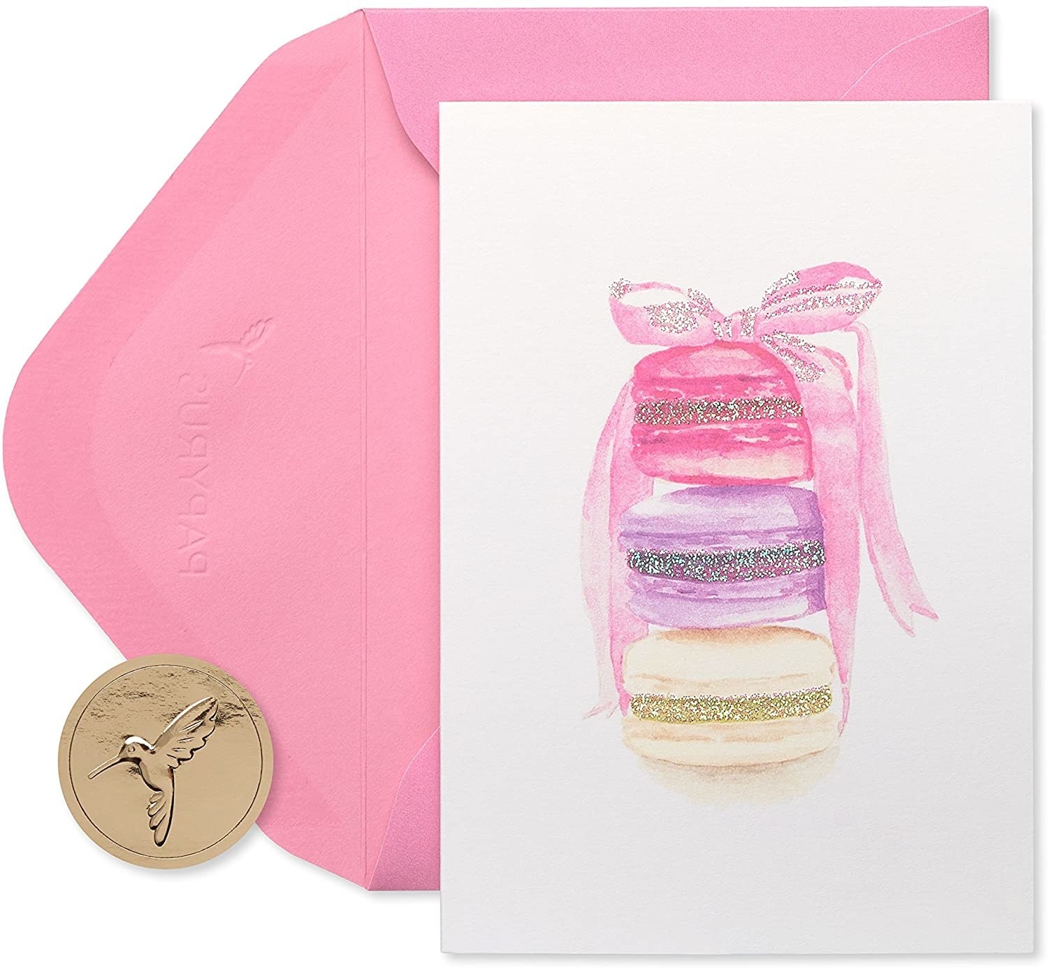 A white card with pastel ivory, purple, and pink watercolor macarons stacked on top of each other with glitter accents in their fillings, plus a pink envelope 