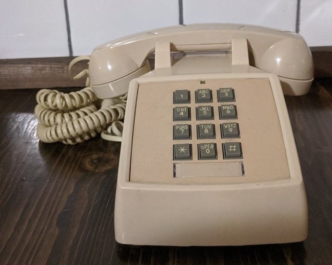 A beige landline phone with push-down gray buttons
