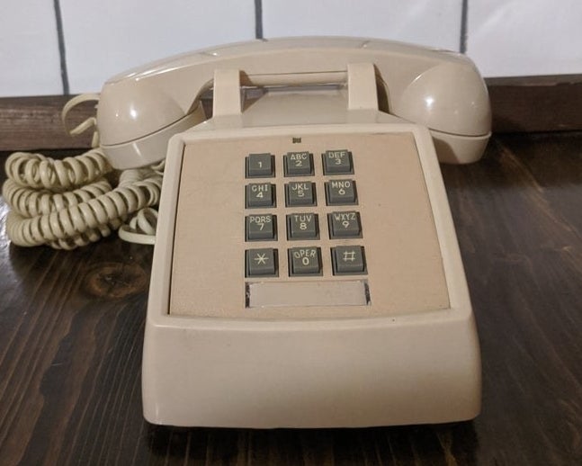 A beige landline phone with push-down gray buttons