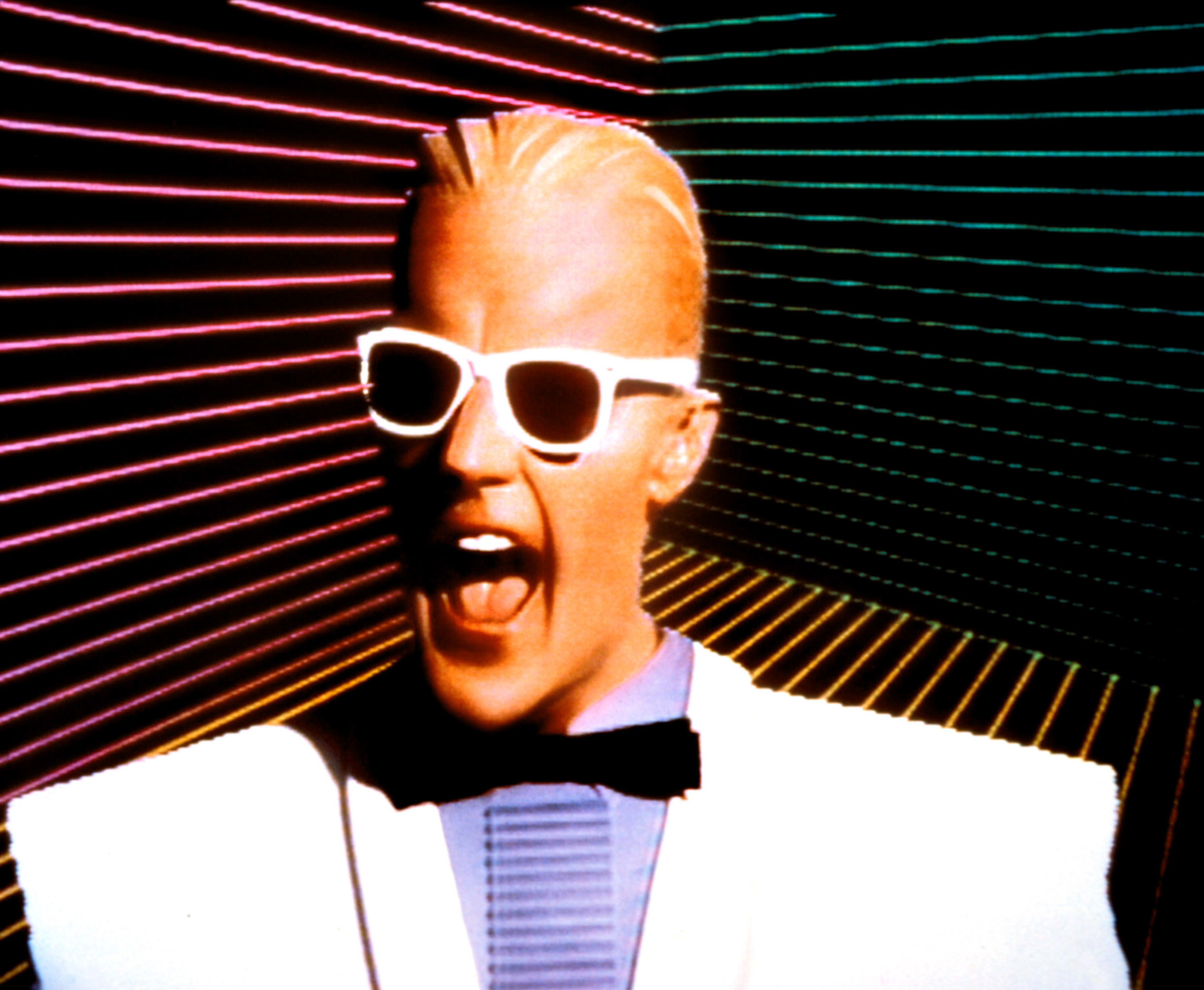 A promotional photo of Max Headroom wearing white Wayfarer sunglasses and a white suite with large shoulder pads