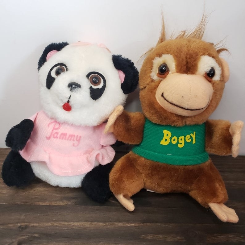 A stuffed animal of Pammy Panda in a pink dress and Bogey Orangutan in a green T-shirt