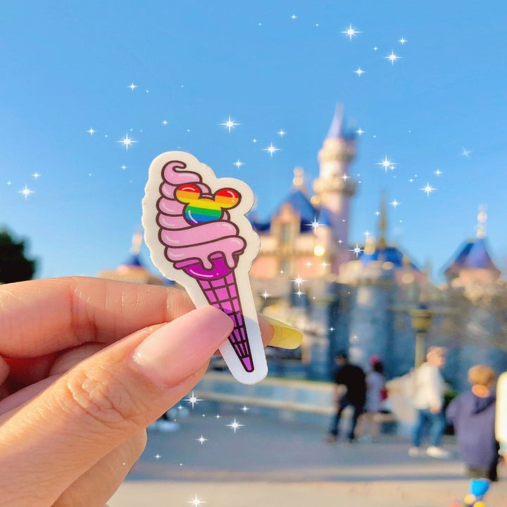 A sticker of a pink ice cream cone with a rainbow Mickey mouse embedded in it 