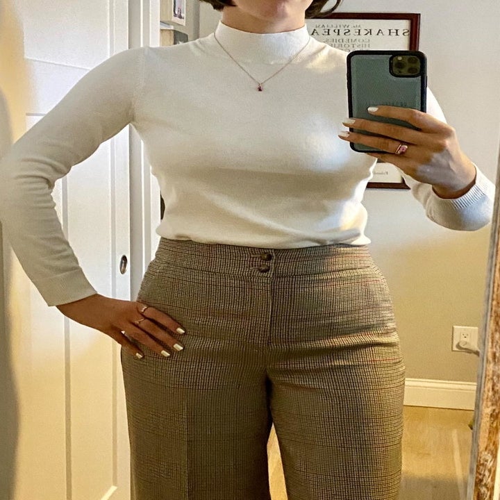 A mirror selfie of a reviewer wearing a cream mock neck sweater tucked into brown pants