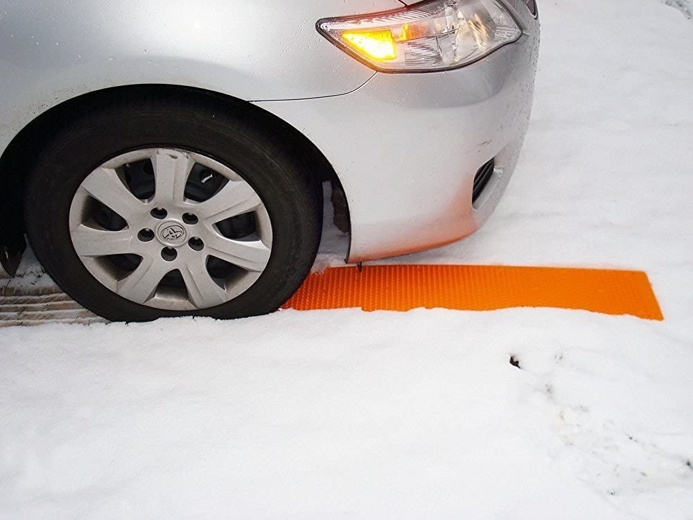 Bright orange grippy mat placed on snow under tire 