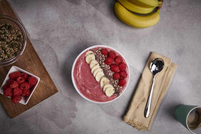 A pink smoothie bowl topped with raspberries, sliced banana, and seeds