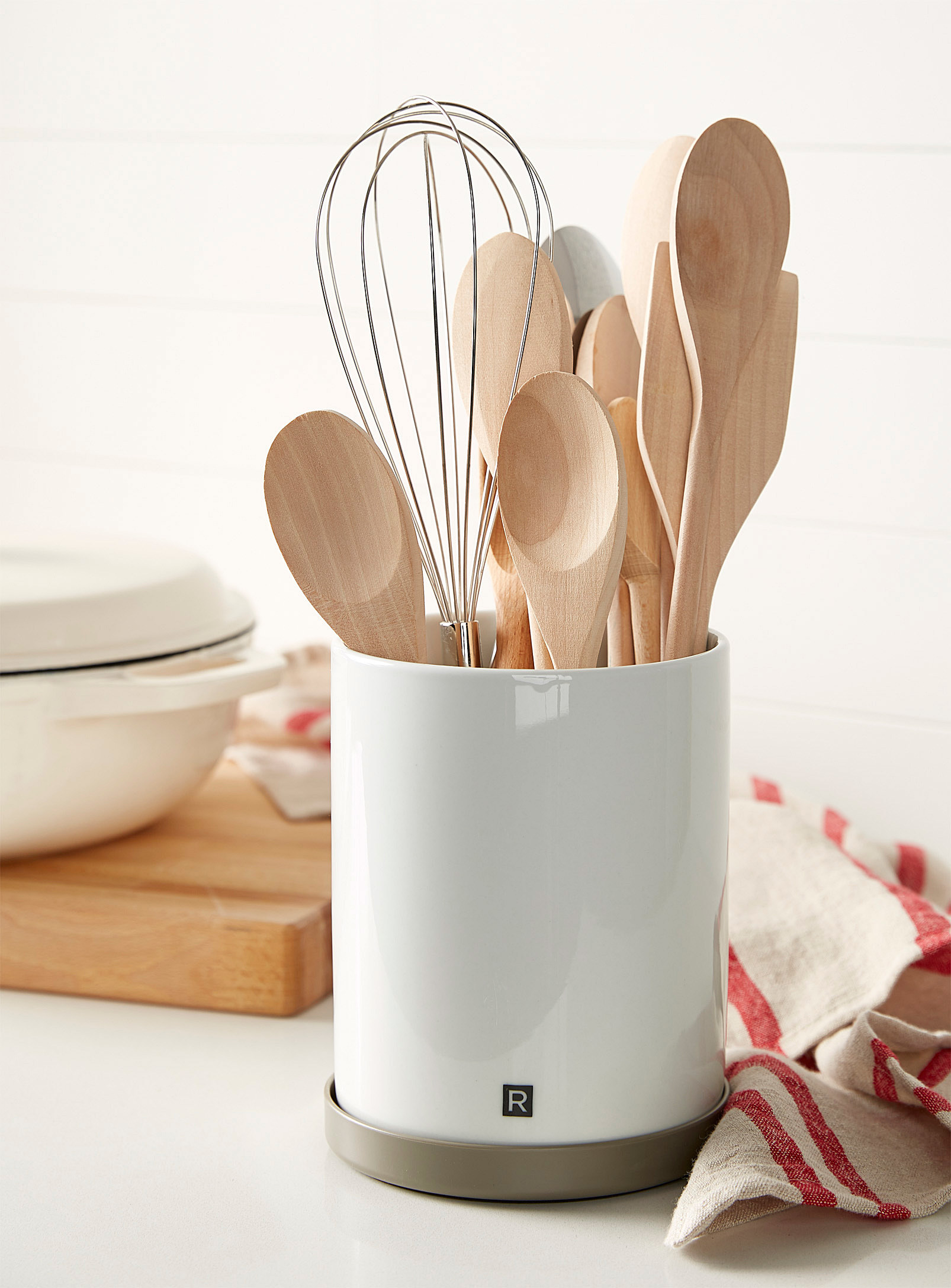 A large porcelain utensil holder filled with wooden spoons and a whisk