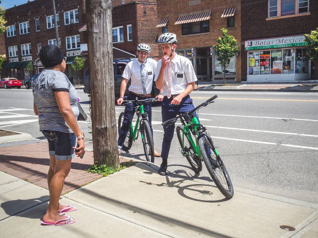 Two men in ties on bikes talk to a woman on the sidewalk