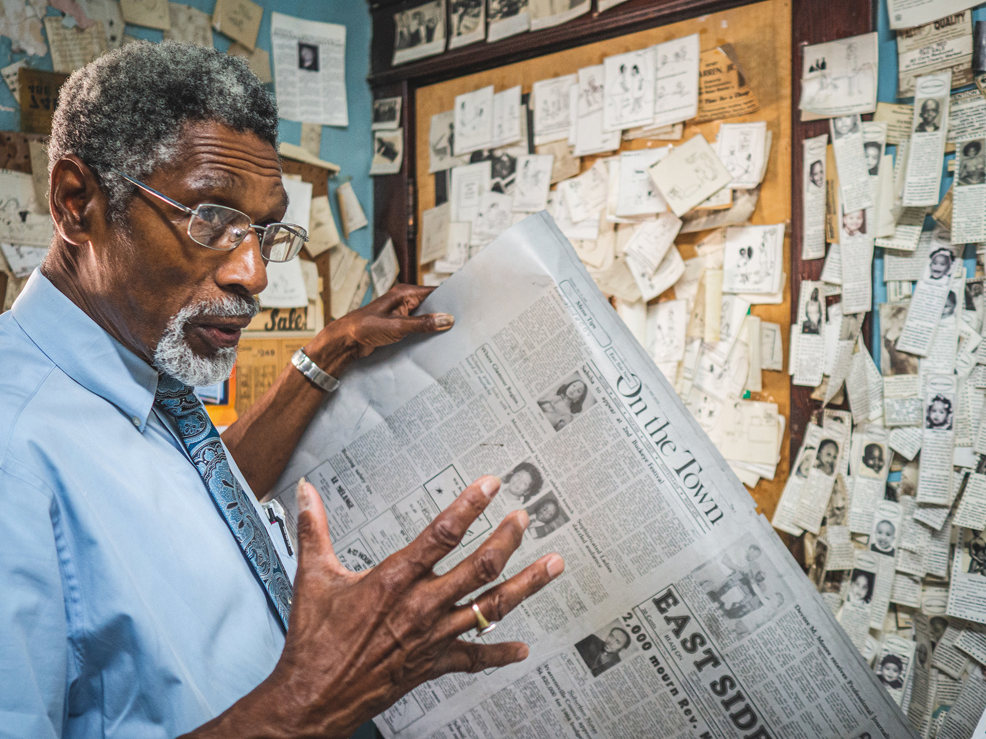 A man holds a newspaper in front of a wall filled with notes