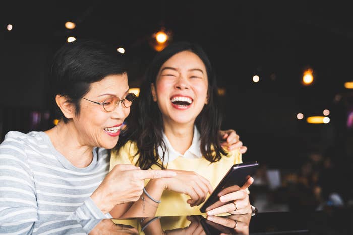 A young Asian woman and her mother laughing at something on the young woman's phone.