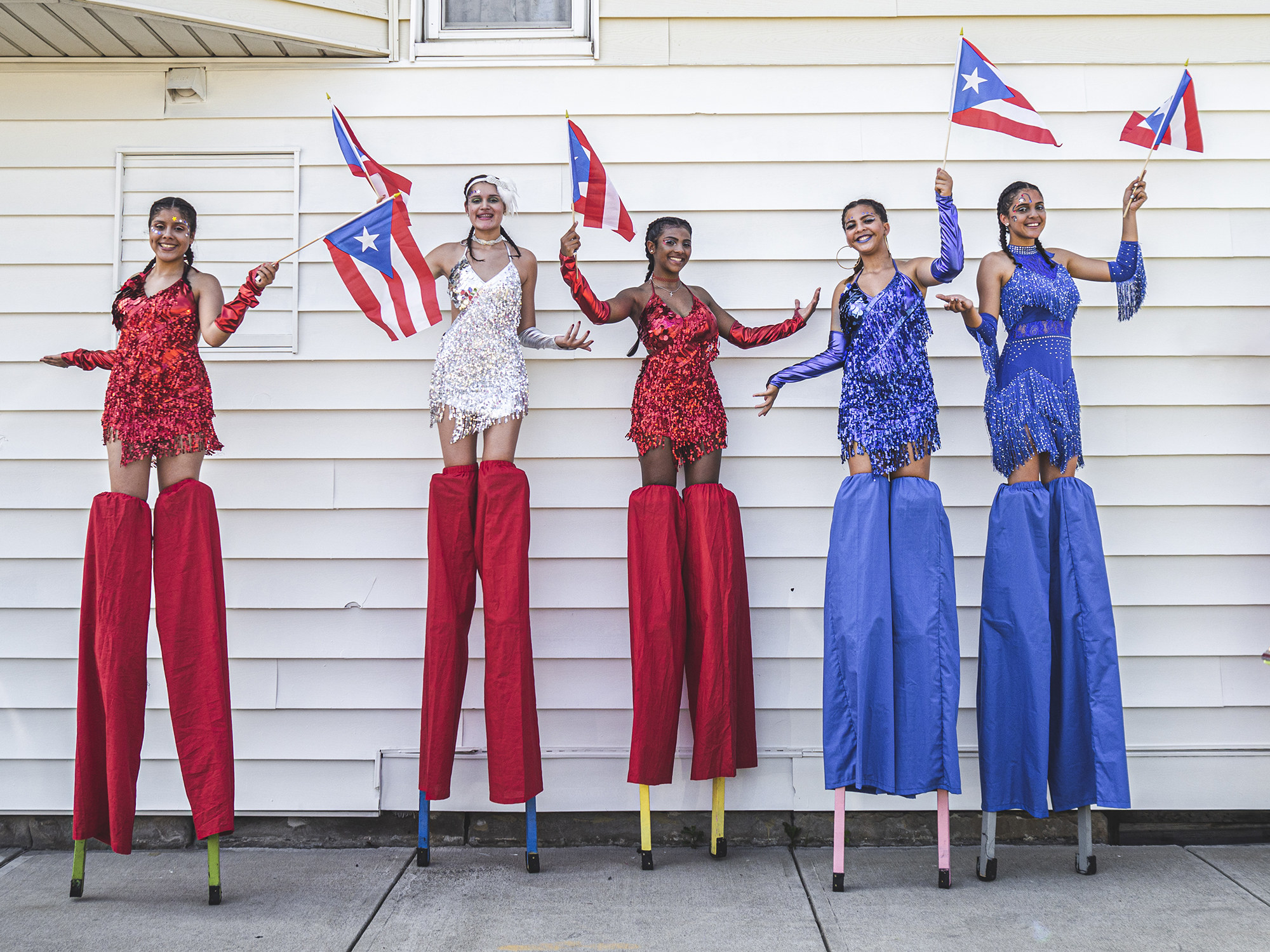 Five women on stilts holding Puerto Rican flags