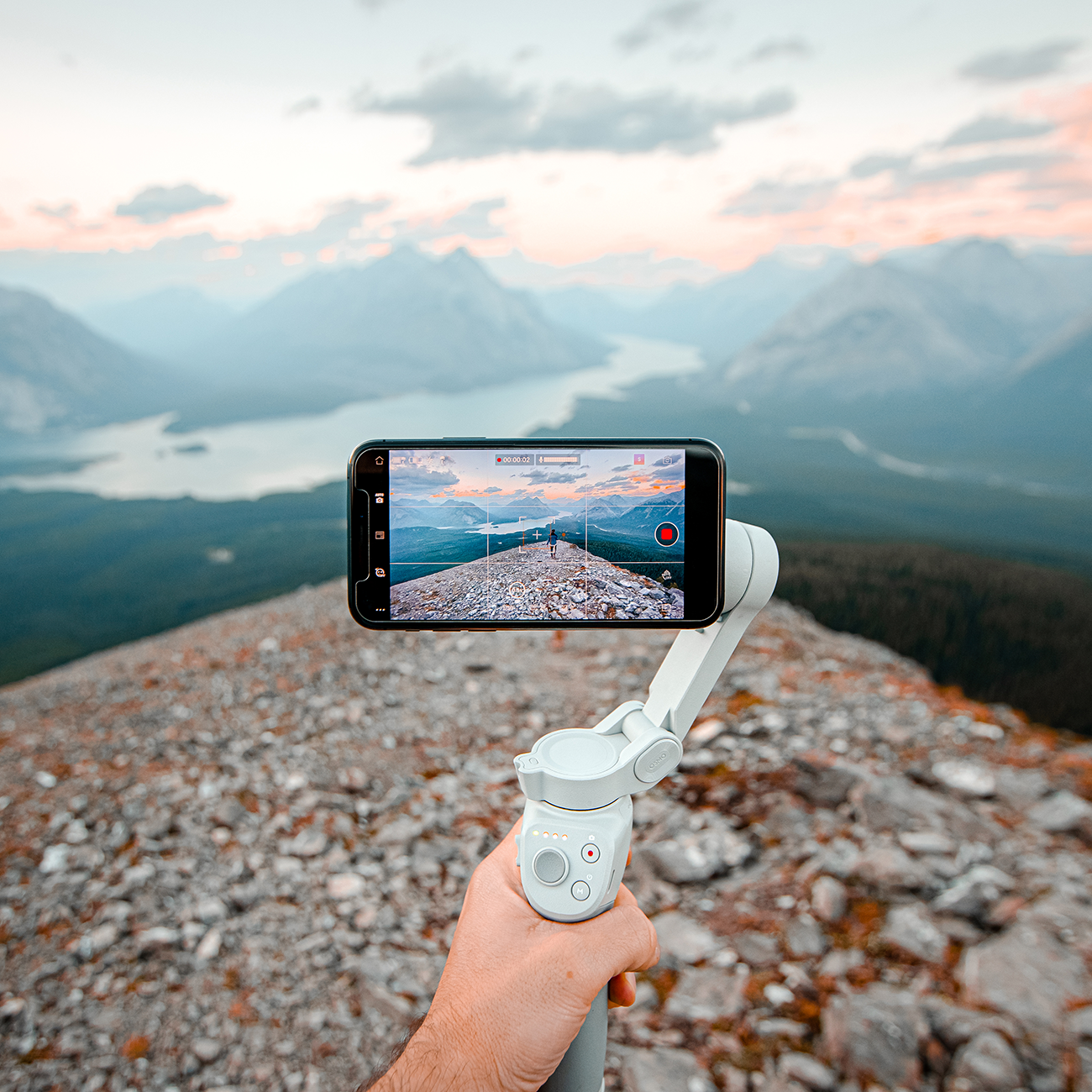 A hand holding up an OM 4 to capture a mountainous skyline