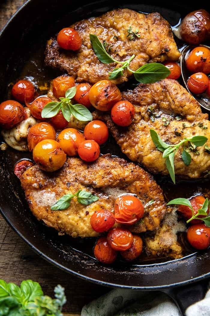Breaded chicken breasts with burst cherry tomatoes and basil in a skillet