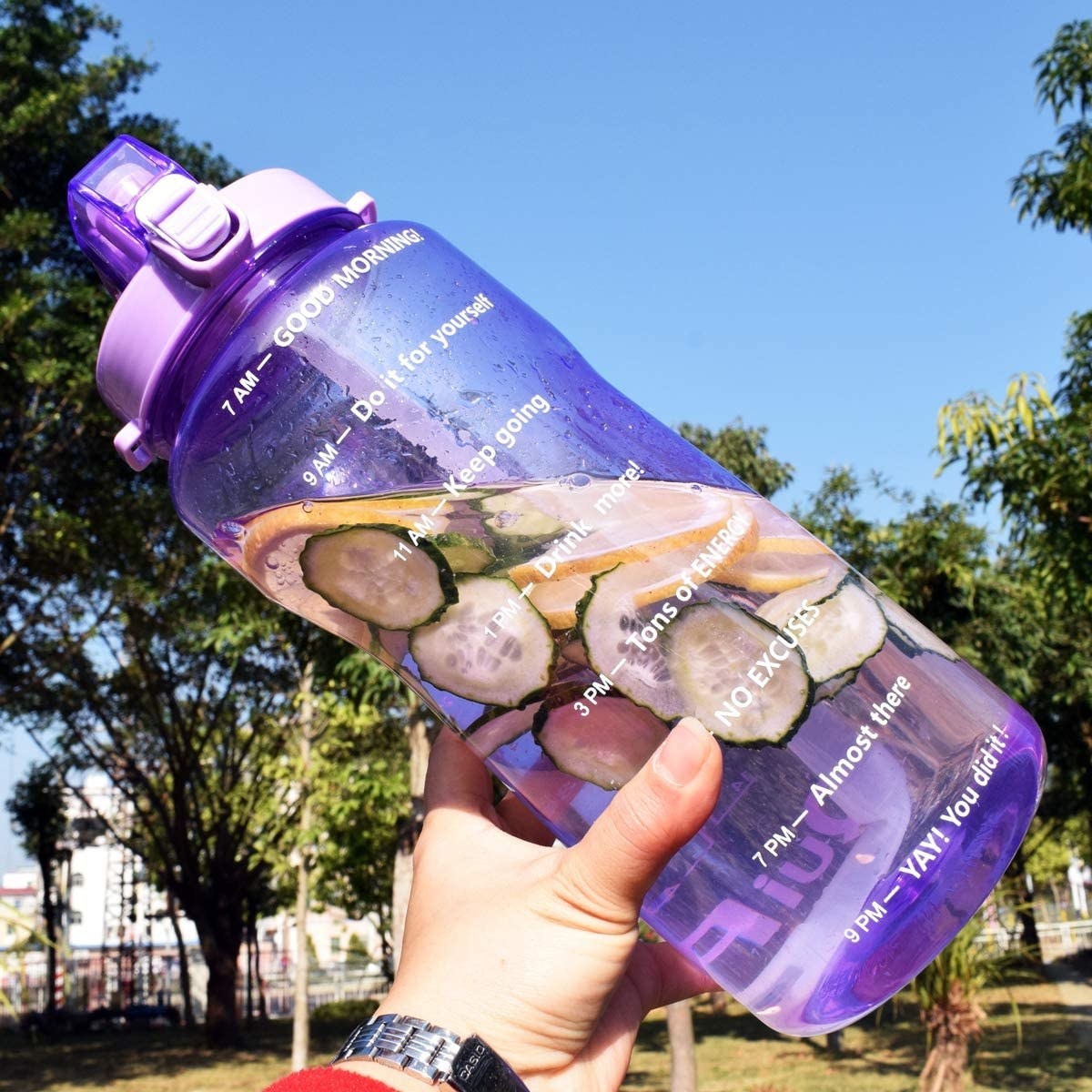 A person holding the water bottle, it's filled with cucumber and lemon slices