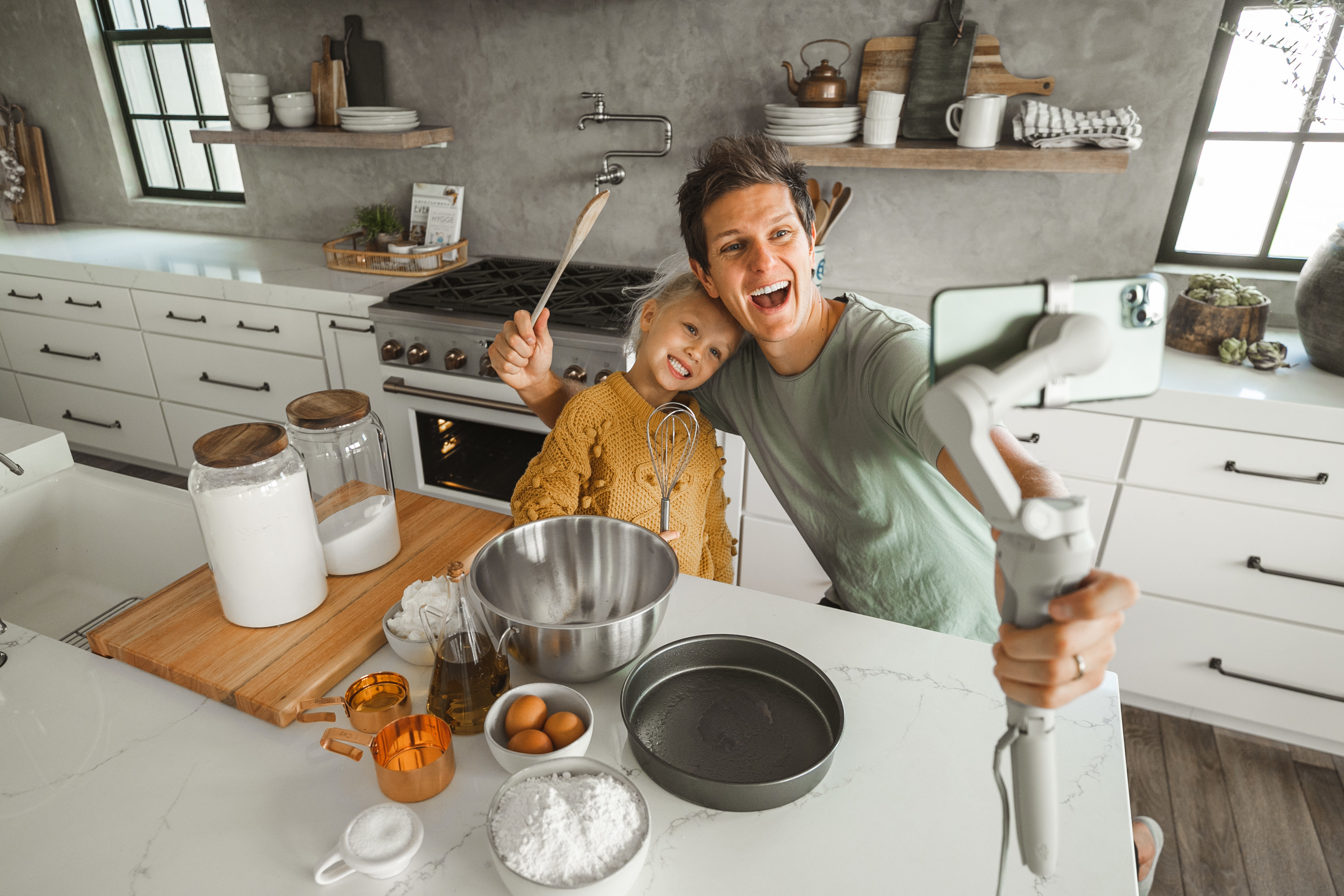 A father taking a video selfie with his daughter behind cooking ingredients