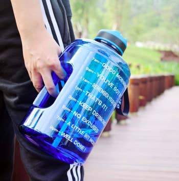 Hand holds blue motivational water bottle with time markers and words of encouragement printed on the side