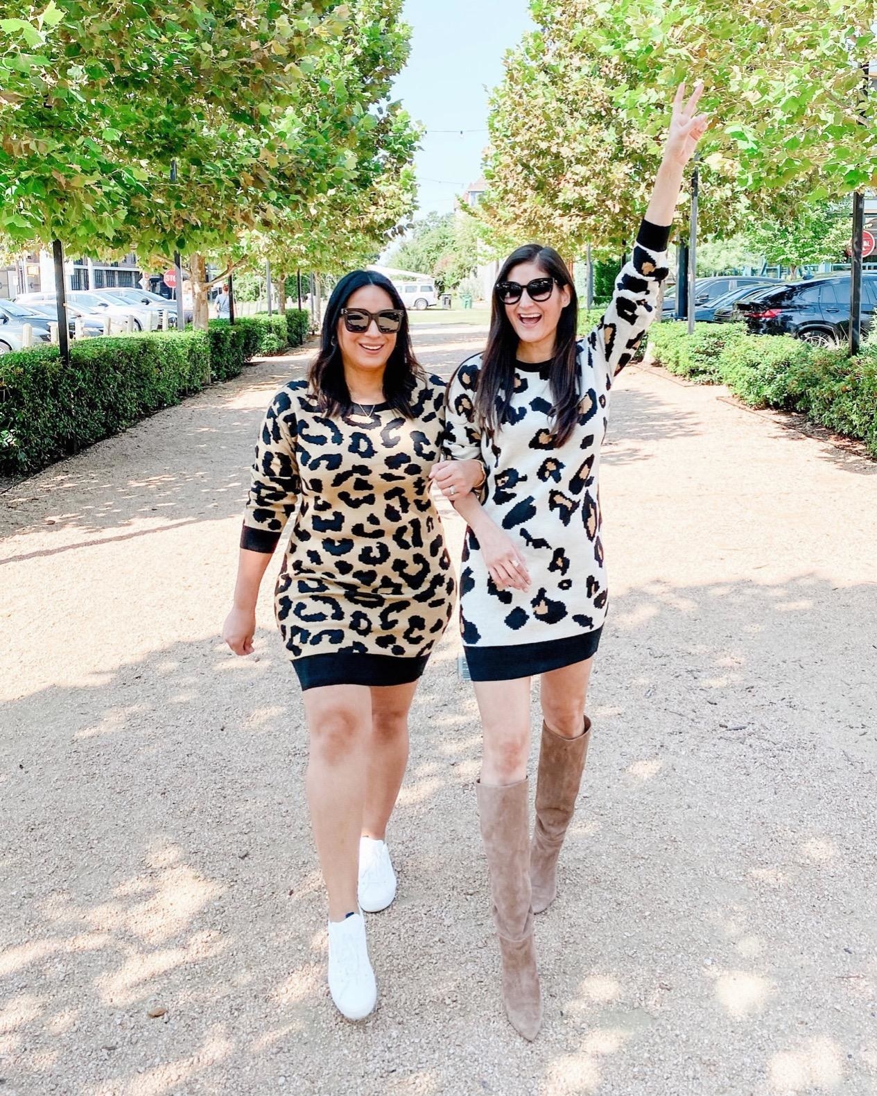 A reviewer wearing a cheetah print sweater dress with sneakers while walking alongside a friend in a similar dress with boots