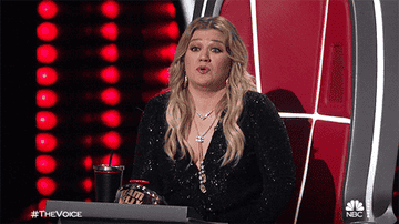gif of Kelly Clarkson on the TV show &quot;The Voice&quot; shrugging her shoulders and raising her hands